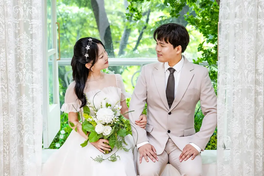 창가 커튼 앞에 나란히 선 두 사람