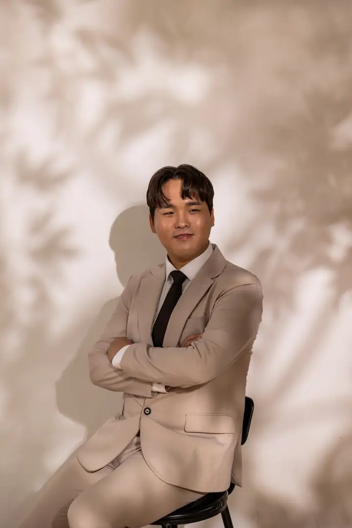 나뭇잎 그림자 벽 앞 의자에 팔짱 끼고 앉아 웃는 신랑 지호