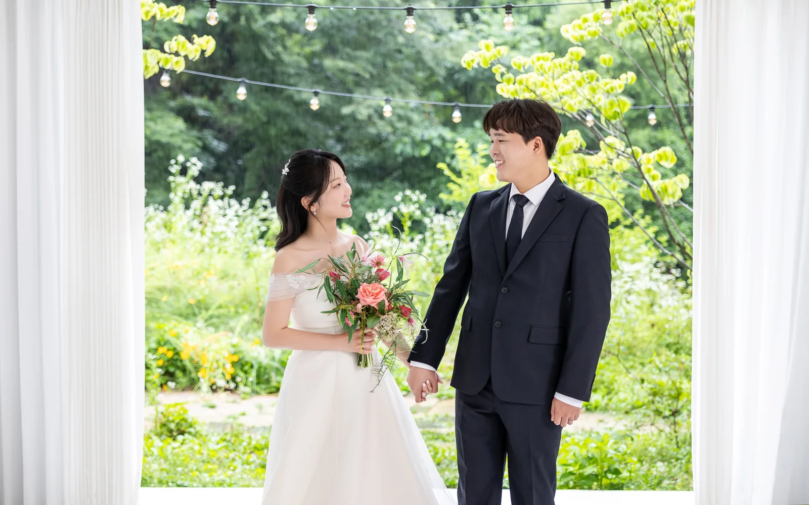 커튼 사이 초록 정원 앞에서 마주 보는 두 사람